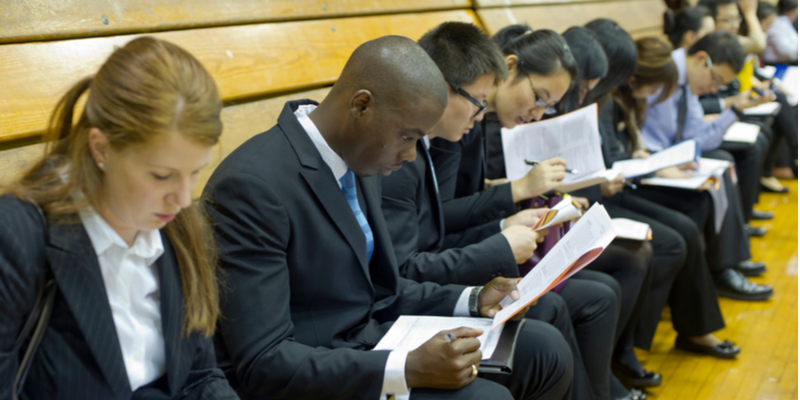 professionally dressed candidates seated in a row and filling up the form to attend the H1B visa interview