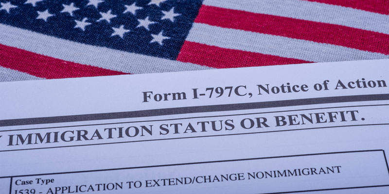 The Form I - 797C (Application to extend change of nonimmigrant status) on a background of the national flag of the United States of America