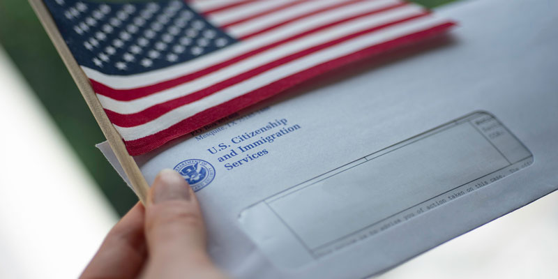Hands holding a flag of the USA and an envelope from USCIS (United States Citizenship and Immigration Services)