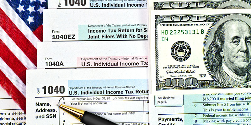 Tax forms 1040 with a pen and the US hundred-dollar bills on the American flag background