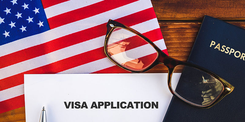 Flag of the United States, visa application form with a pen , specs and a passport are on the wooden table