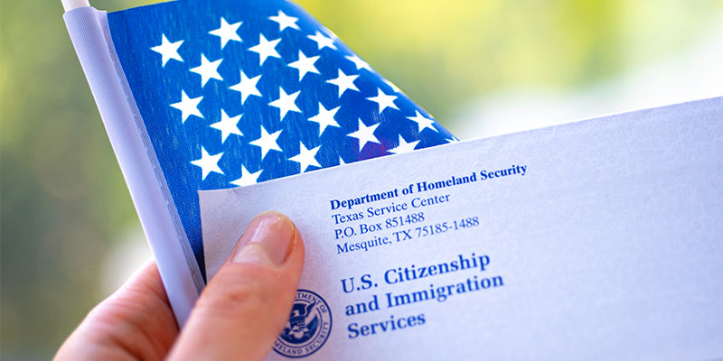 Holding an American flag and a letter with the logo of U.S. citizenship and immigration services and the department of homeland security's address