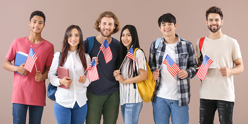 Group of young students of different nationalities holding USA flag in their hands