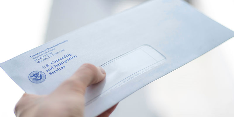 An envelope from USCIS (United States citizenship and immigration services) in hand, blurry on a white background.