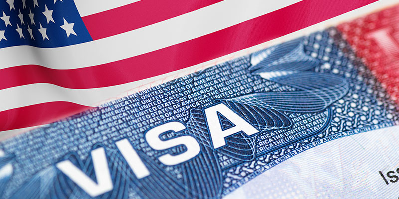 A closeup of the H1B visa stamp over the background of a waving American flag