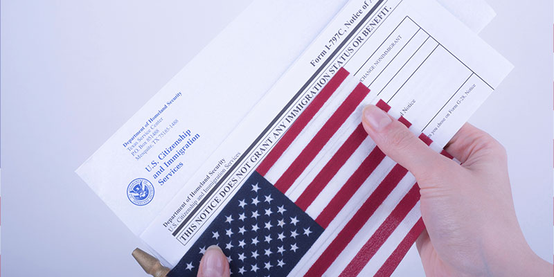 Hands holding a US citizenship and immigration services envelope, along with I - 797C - white form and the flag of the USA .