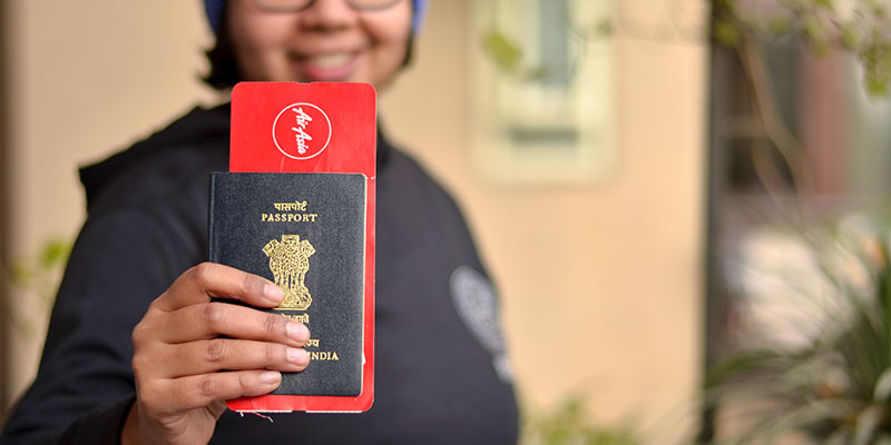 A young woman wearing specs and a blue cap holding an Indian passport and air ticket. Selective focus on the passport and ticket her face is blurred.